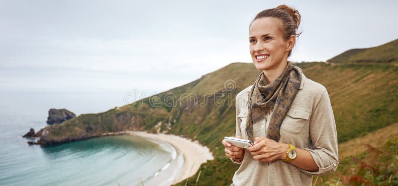 Les sms heureux d'écriture de randonneur de femme devant la vue d'océan aménagent en parc image libre de droits Les sms heureux d'écriture de randonneur de femme devant la vue d'océan aménagent en parc image libre de droits