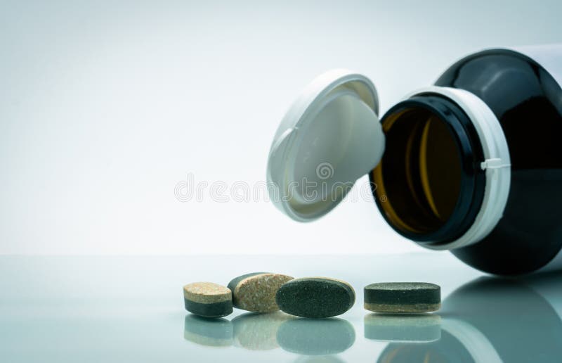 Essential Vitamins and minerals supplements dual layer tablet pills and medicine glass bottle with open cap isolated on white background with copy space. Use for vitamins and supplements advertising. Essential Vitamins and minerals supplements dual layer tablet pills and medicine glass bottle with open cap isolated on white background with copy space. Use for vitamins and supplements advertising.