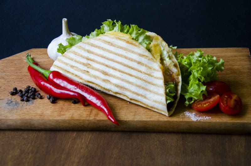 Les tacos mexicains avec de la viande, la salade et des légumes de poulet sauce présenté sur un conseil en bois avec une tomate f photo stock Les tacos mexicains avec de la viande, la salade et des légumes de poulet sauce présenté sur un conseil en bois avec une tomate f photo stock
