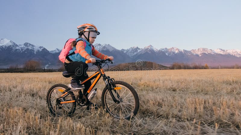 Les tours caucasiens des enfants un font du vélo dans le domaine de blé Cycle orange de noir d'équitation de petite fille sur le photo libre de droits Les tours caucasiens des enfants un font du vélo dans le domaine de blé Cycle orange de noir d'équitation de petite fille sur le photo libre de droits