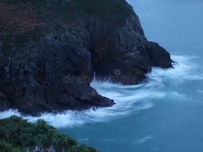 Les vagues entourant les rochers de la côte provoquent des éclaboussures et des mousses. Lorsque les vagues atteignent la côte, elles entrent en collision avec les gros rochers des montagnes de l'espagne du nord dans les asturias, provoquant des nuances de couleur différentes qui se déplacent entre le blanc et le bleu en contraste avec la couleur foncée des roches volcaniques