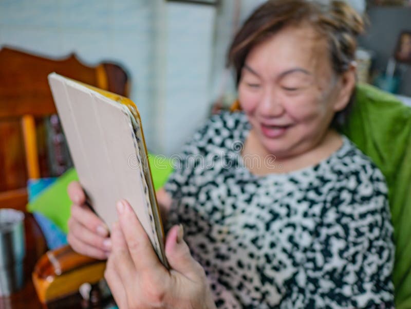 Les vieilles femmes asiatiques très heureuses regardent le comprimé dans sa maison, vieux c photographie stock Les vieilles femmes asiatiques très heureuses regardent le comprimé dans sa maison, vieux c photographie stock