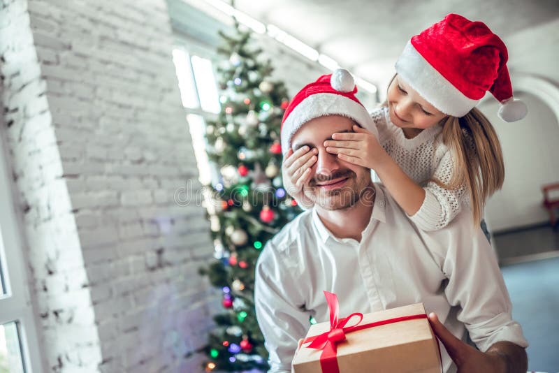Les yeux du père se fermant de fille joyeuse mignonne avec la main donnant le boîte-cadeau photo libre de droits Les yeux du père se fermant de fille joyeuse mignonne avec la main donnant le boîte-cadeau photo libre de droits
