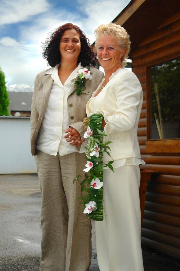 Matura coppia di lesbiche in posa e tenendo le mani in cerimoniale abito formale con bouquet dopo la cerimonia nuziale in grande stile.