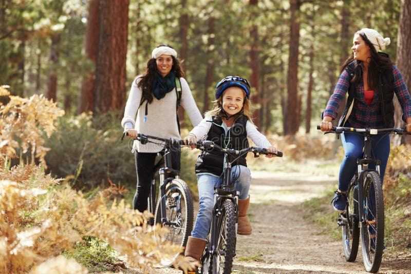 Lesbian couple cycling in a forest with their daughter royalty free stock photography