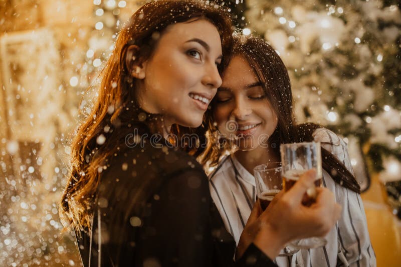 Lesbian Couple Holds Glasses Of Wine Against Background Of Christmas