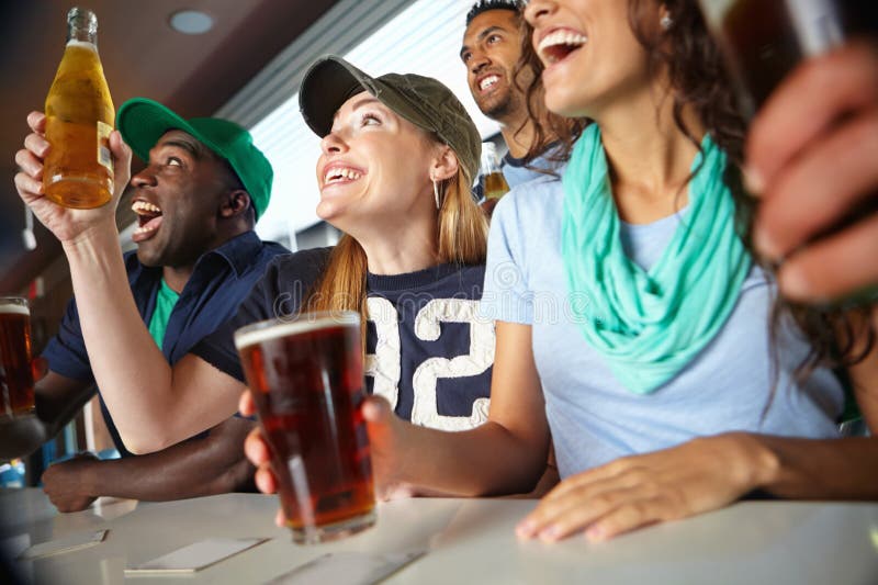 Let the good times roll. A beautiful woman cheering on her favourite team with friends at the bar.