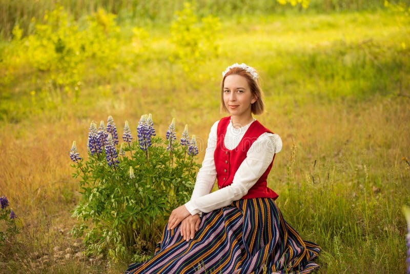 Latvian woman in traditional clothing with blue lupine flowers posing in field on nature background in village. Ligo festival. Riga. Latvia. Latvian woman in traditional clothing with blue lupine flowers posing in field on nature background in village. Ligo festival. Riga. Latvia