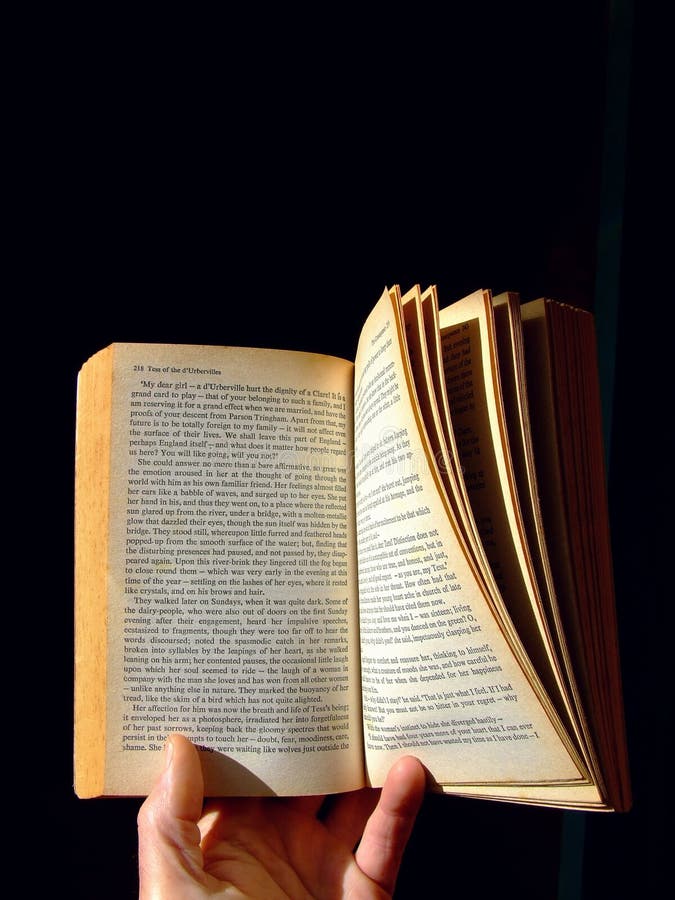 A thick, old paperback novel held open in one hand and lit by sunlight against deep shadow. (The book is Tess of the d'Urbervilles by Thomas Hardy, first published 1891.). A thick, old paperback novel held open in one hand and lit by sunlight against deep shadow. (The book is Tess of the d'Urbervilles by Thomas Hardy, first published 1891.)