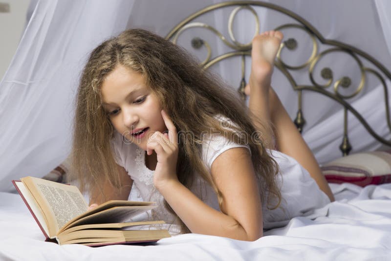 Leuk een boek lezen en meisje die terwijl het liggen op een bed in de ruimte glimlachen royalty-vrije stock foto Leuk een boek lezen en meisje die terwijl het liggen op een bed in de ruimte glimlachen royalty-vrije stock foto