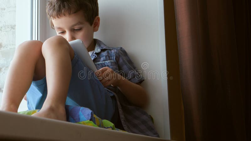 Leuk gebruikt weinig jongen een witte tabletpc thuis op een vensterbank royalty-vrije stock foto's Leuk gebruikt weinig jongen een witte tabletpc thuis op een vensterbank royalty-vrije stock foto's