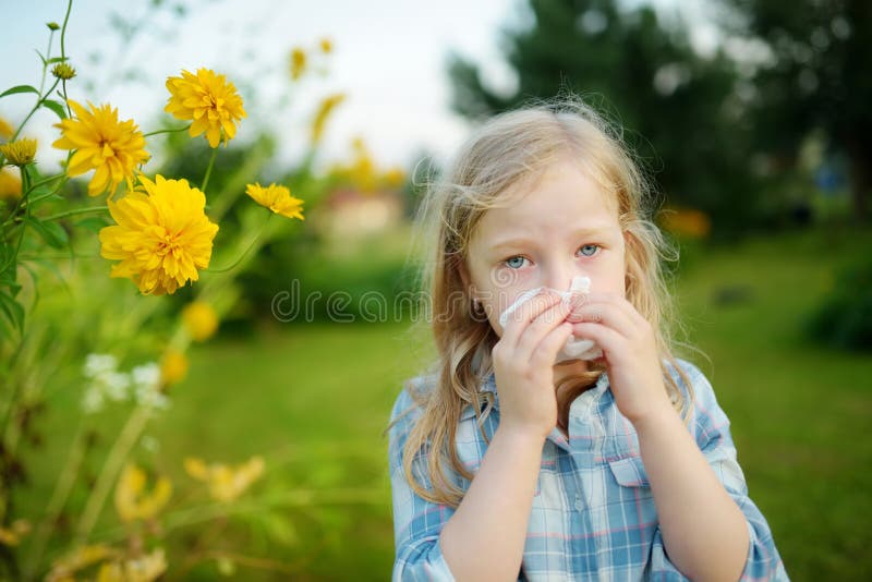 Leuk meisje die haar neus blazen door mooie gele coneflowers op de zomerdag Allergie en astmakwesties in kleine jonge geitjes