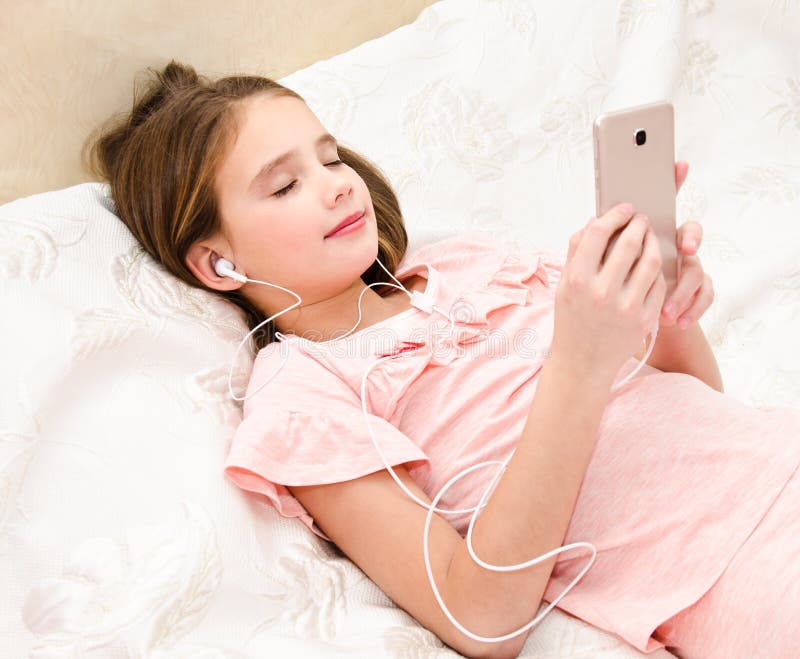 Leuk meisje die op het bed liggen en aan muziek luisteren die s gebruiken royalty-vrije stock afbeeldingen Leuk meisje die op het bed liggen en aan muziek luisteren die s gebruiken royalty-vrije stock afbeeldingen