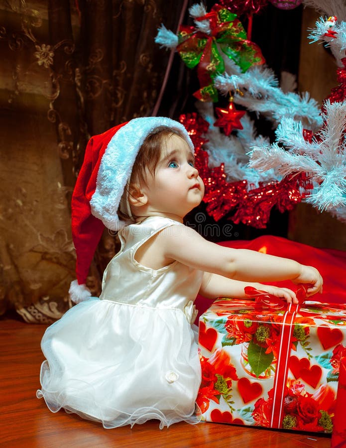 Cute little baby girl in Stana hat opens her first Christmas present. New year. Christmas mood. Cute little baby girl in Stana hat opens her first Christmas present. New year. Christmas mood.