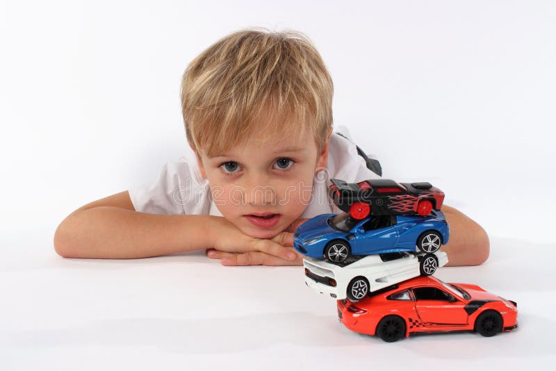 Leuk preteen jongen het liggen met een stapel van autospeelgoed en het maken van een verwarde blik in zijn gezicht stock afbeelding Leuk preteen jongen het liggen met een stapel van autospeelgoed en het maken van een verwarde blik in zijn gezicht stock afbeelding