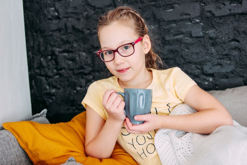 Leuk tween meisje in gele t-shirt met kop tes in bed, comfortabel huis royalty-vrije stock afbeelding Leuk tween meisje in gele t-shirt met kop tes in bed, comfortabel huis royalty-vrije stock afbeelding