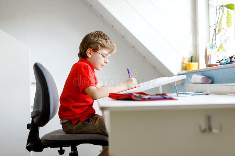 Leuk weinig jong geitjejongen met glazen die thuis thuiswerk maken, schrijvend brieven met kleurrijke pennen stock foto Leuk weinig jong geitjejongen met glazen die thuis thuiswerk maken, schrijvend brieven met kleurrijke pennen stock foto