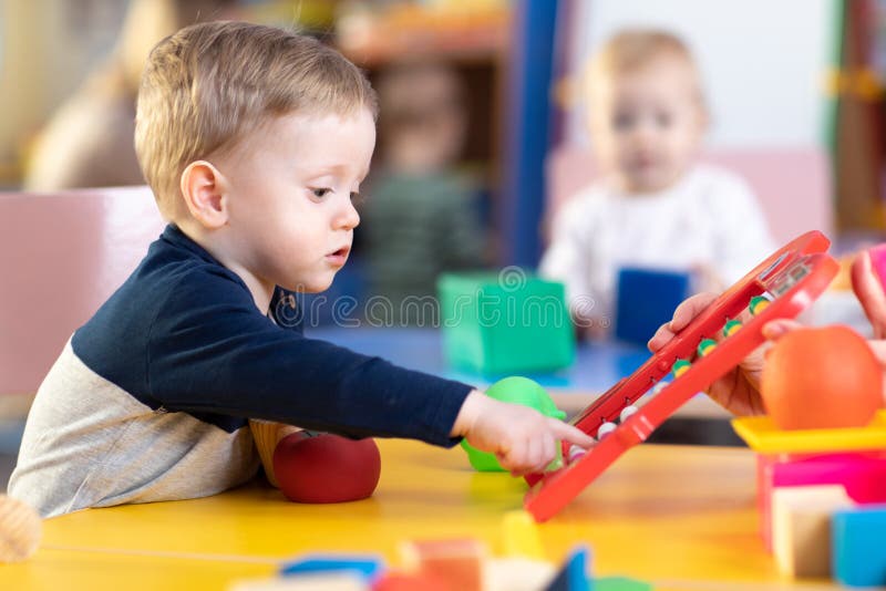 Leuk weinig jongen die met telraam in kinderdagverblijf spelen Kleuter die pret met onderwijsstuk speelgoed in opvang of kleuters royalty-vrije stock foto Leuk weinig jongen die met telraam in kinderdagverblijf spelen Kleuter die pret met onderwijsstuk speelgoed in opvang of kleuters royalty-vrije stock foto