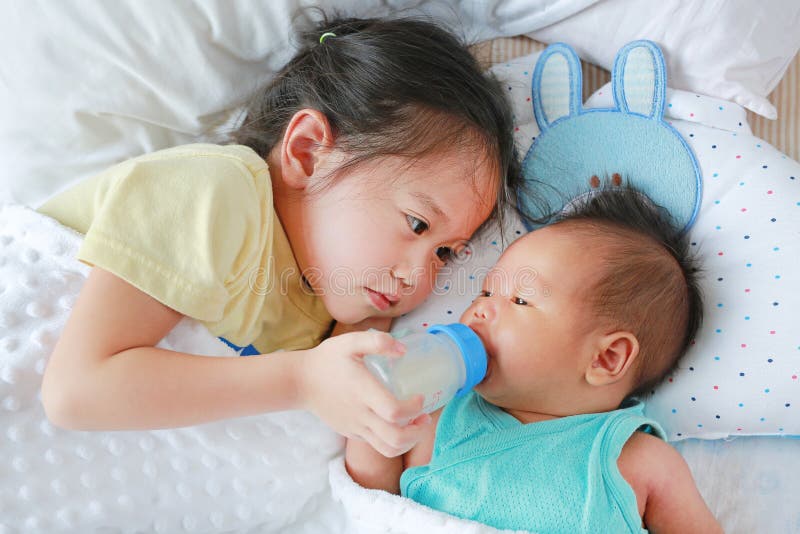 Leuke Aziatische zuster het voeden melk van fles voor het pasgeboren baby liggen op het bed royalty-vrije stock afbeeldingen Leuke Aziatische zuster het voeden melk van fles voor het pasgeboren baby liggen op het bed royalty-vrije stock afbeeldingen