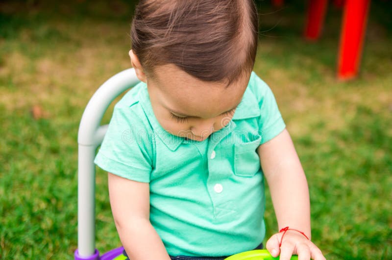 Leuke babyjongen die turkooise t-shirt en gekamd haar dragen, die buiten op grasrijke oppervlakte zitten die rond spelen stock afbeeldingen Leuke babyjongen die turkooise t-shirt en gekamd haar dragen, die buiten op grasrijke oppervlakte zitten die rond spelen stock afbeeldingen