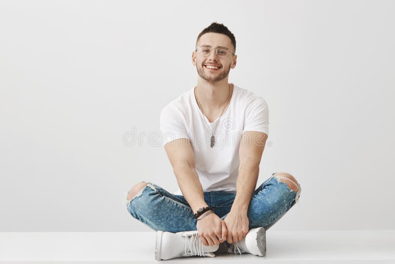 Leuke en in vriend die in glazen op vloer met gekruiste benen zitten, houdend handen op voeten, die ruim glimlachen bij royalty-vrije stock foto Leuke en in vriend die in glazen op vloer met gekruiste benen zitten, houdend handen op voeten, die ruim glimlachen bij royalty-vrije stock foto