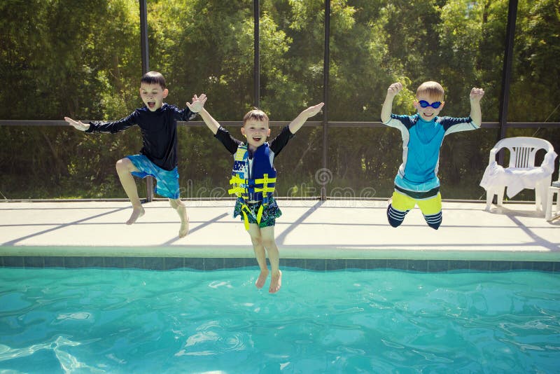 Cute young boys jumping into an outdoor swimming pool while on a fun vacation. Fun expressions as they dive into the water together. Cute young boys jumping into an outdoor swimming pool while on a fun vacation. Fun expressions as they dive into the water together