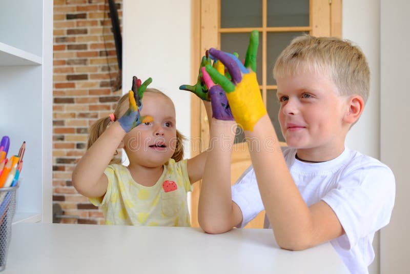 Leuke jongen die met geschilderde handen met zijn kleine zuster thuis spelen royalty-vrije stock foto's Leuke jongen die met geschilderde handen met zijn kleine zuster thuis spelen royalty-vrije stock foto's