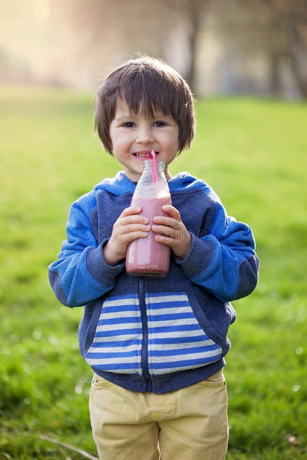 Leuke jongen, het drinken gezonde aardbei smoothie in het park royalty-vrije stock fotografie Leuke jongen, het drinken gezonde aardbei smoothie in het park royalty-vrije stock fotografie