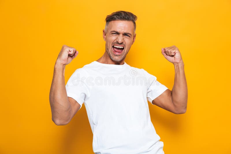 Levantamento entusiasmado feliz do homem isolado sobre o fundo amarelo da parede para fazer o gesto do vencedor foto de stock Levantamento entusiasmado feliz do homem isolado sobre o fundo amarelo da parede para fazer o gesto do vencedor foto de stock