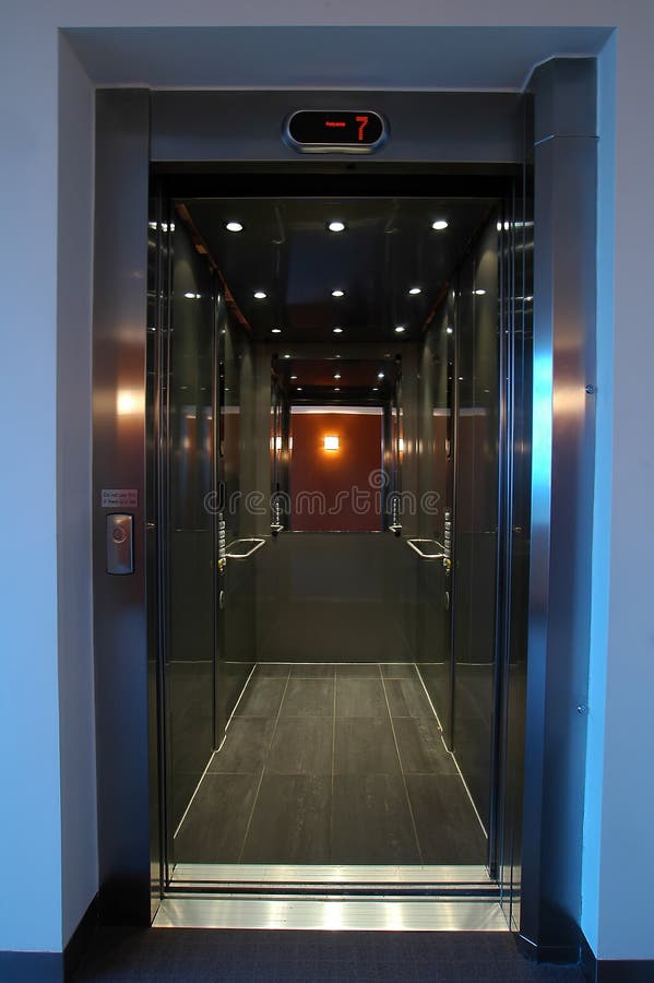 Open stainless elevator with mirror, mirror reflects orange wall, level 7. Open stainless elevator with mirror, mirror reflects orange wall, level 7