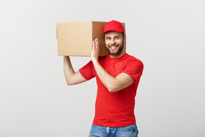 Lever Concept: Jonge Kaukasische knappe leveringsmens die een doos op schouder houden Geïsoleerdg over grijze achtergrond stock foto Lever Concept: Jonge Kaukasische knappe leveringsmens die een doos op schouder houden Geïsoleerdg over grijze achtergrond stock foto