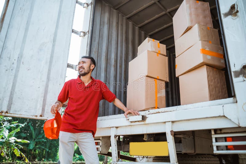 Leveransman som väntar på order om att lyfta pappkartonger bakom containerlastbil som bakgrund