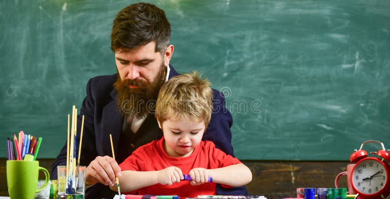 Lezione di arte all'asilo Insegnante che aiuta il ragazzo a creare immagine Equipaggi la pittura con la spazzola lunga mentre il fotografia stock libera da diritti Lezione di arte all'asilo Insegnante che aiuta il ragazzo a creare immagine Equipaggi la pittura con la spazzola lunga mentre il fotografia stock libera da diritti