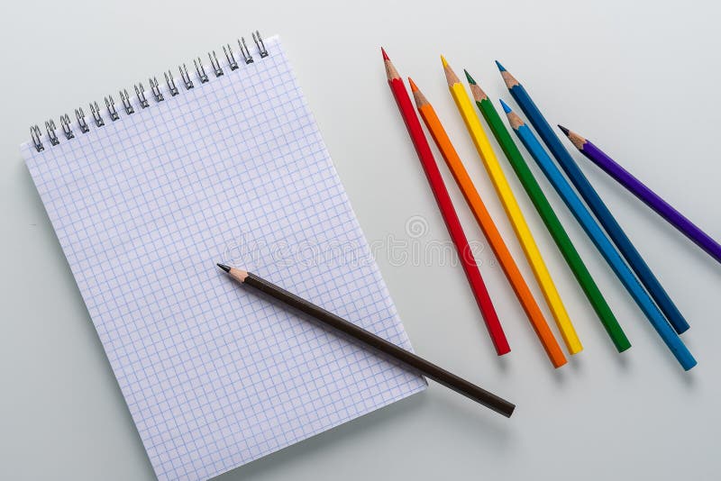 Libreta limpia en una jaula con un lápiz que miente en él y los lápices del color del arco iris en un espacio blanco de la copia fotos de archivo libres de regalías Libreta limpia en una jaula con un lápiz que miente en él y los lápices del color del arco iris en un espacio blanco de la copia fotos de archivo libres de regalías