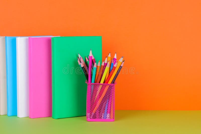 Libri e un vetro con le matite colorate su un fondo arancio e verde con un posto per scrivere fotografie stock Libri e un vetro con le matite colorate su un fondo arancio e verde con un posto per scrivere fotografie stock