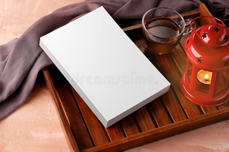 Libro blanco en blanco con té y lámpara para maquetas en una bandeja de madera