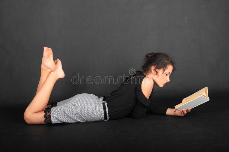 Concentrated teenage girl - smart schoolkid with brunette hair dressed in black blouse and grey skirt reading an old book. School and education concept. Concentrated teenage girl - smart schoolkid with brunette hair dressed in black blouse and grey skirt reading an old book. School and education concept.