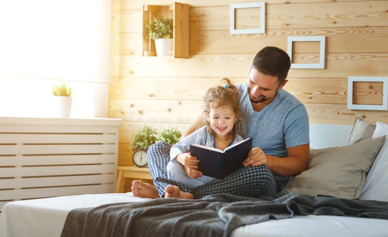 Libro de lectura feliz del padre y de la hija de la familia en cama