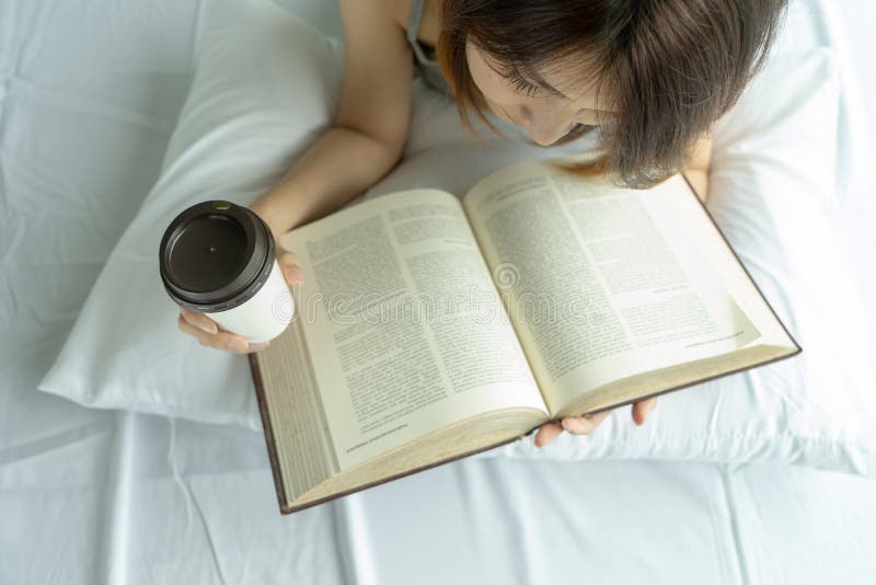 Libro de lectura de la mujer joven con la taza de café de la mañana en dormitorio en casa Opinión de top asiática del té de la be fotografía de archivo libre de regalías Libro de lectura de la mujer joven con la taza de café de la mañana en dormitorio en casa Opinión de top asiática del té de la be fotografía de archivo libre de regalías