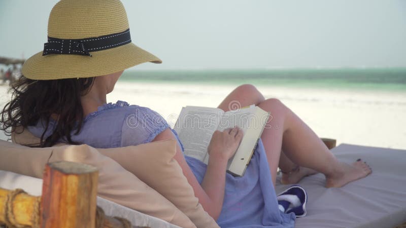 Libro de lectura de la mujer joven en la playa blanca por el océano