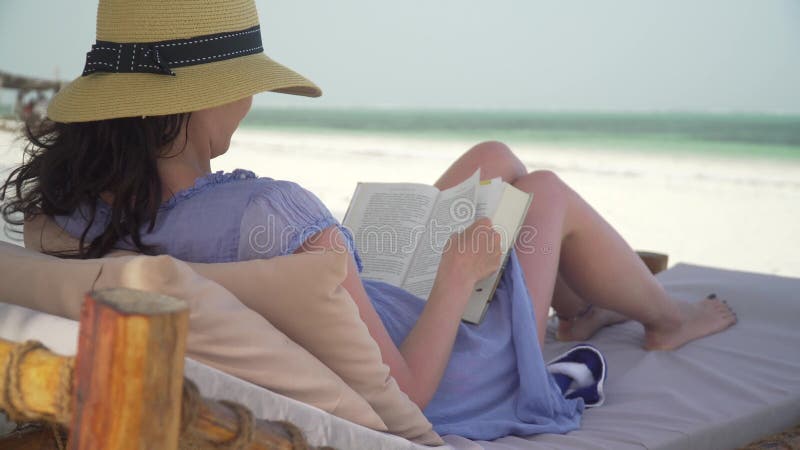 Libro de lectura de la mujer joven en la playa blanca por el océano