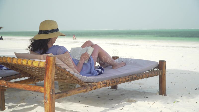 Libro de lectura de la mujer joven en la playa blanca por el océano