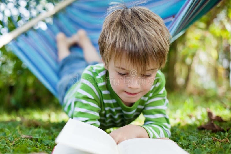 Libro di lettura allegro del ragazzino nell'amaca immagini stock libere da diritti Libro di lettura allegro del ragazzino nell'amaca immagini stock libere da diritti