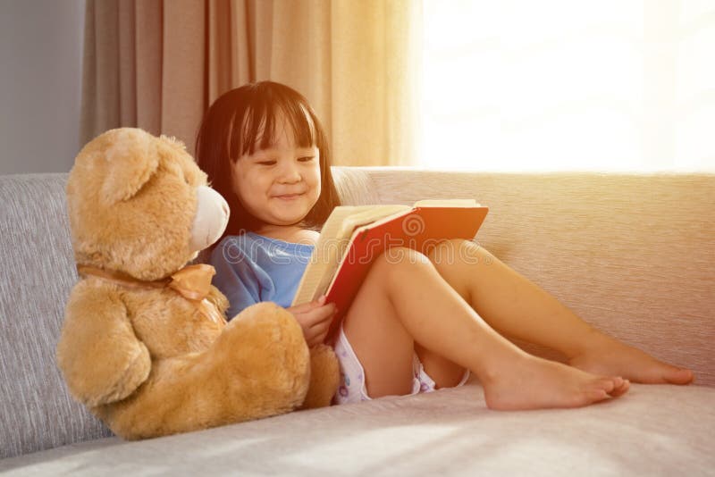 Libro di lettura cinese asiatico sorridente della bambina con l'orsacchiotto