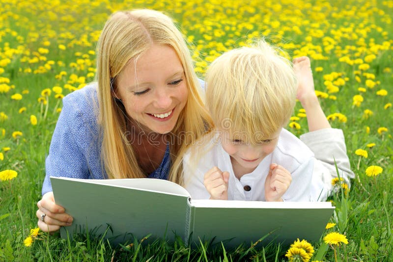 Libro di lettura felice del bambino e della madre fuori in prato fotografia stock libera da diritti Libro di lettura felice del bambino e della madre fuori in prato fotografia stock libera da diritti