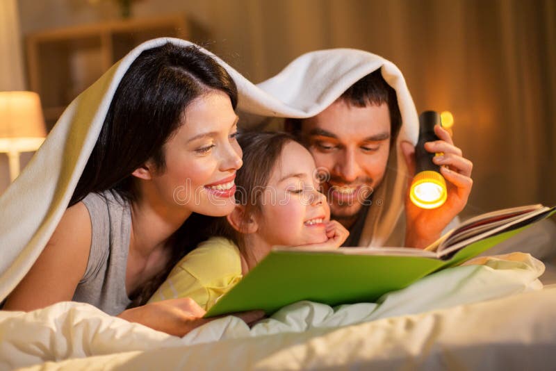 Libro di lettura felice della famiglia a letto alla notte a casa fotografia stock libera da diritti Libro di lettura felice della famiglia a letto alla notte a casa fotografia stock libera da diritti