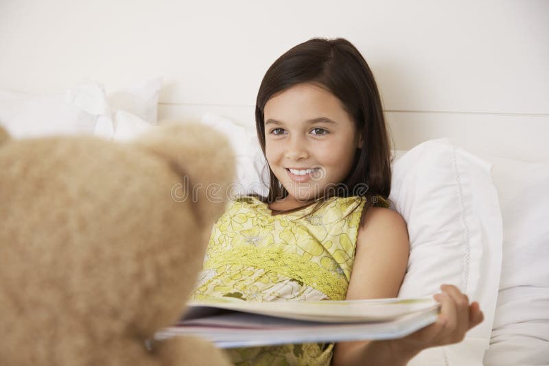 Libro di storia della lettura della ragazza al suo Teddy Bear fotografia stock libera da diritti Libro di storia della lettura della ragazza al suo Teddy Bear fotografia stock libera da diritti