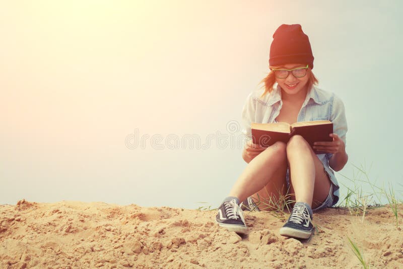 Libro e seduta di lettura della ragazza sulla spiaggia con alba immagini stock libere da diritti Libro e seduta di lettura della ragazza sulla spiaggia con alba immagini stock libere da diritti
