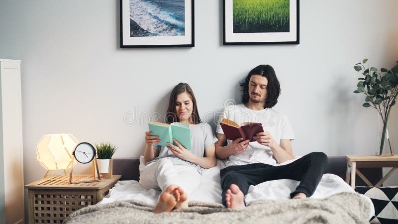 Libros de lectura hermosos de los pares que se sientan en la cama en casa junto que disfruta de la afición