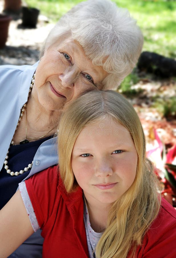 A pretty blond girl and her grandmother in the garden. The little girl looks serious. Vertical view. A pretty blond girl and her grandmother in the garden. The little girl looks serious. Vertical view.